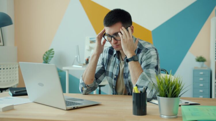 Man holding head in frustration at desk with laptop.