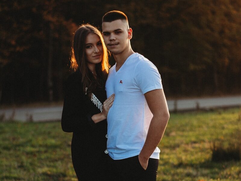 man in white polo shirt and black pants standing beside woman in black pants on green