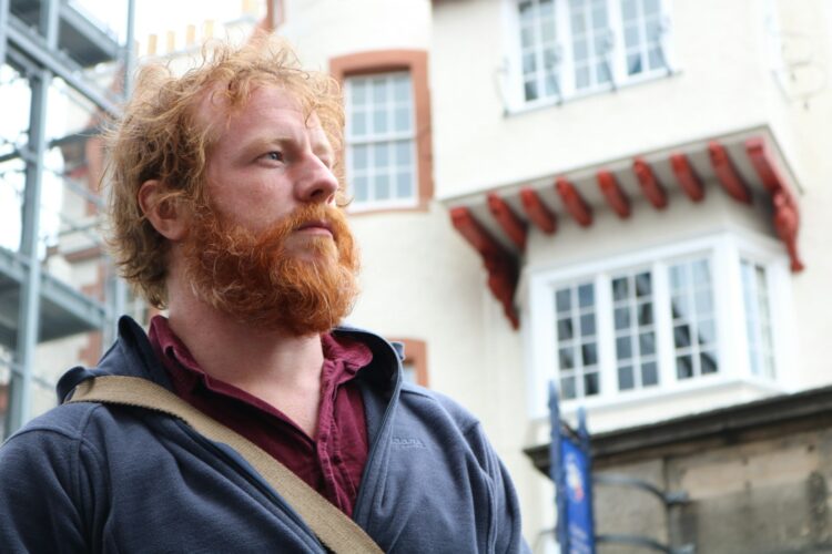 a man with red hair and a beard standing in front of a building