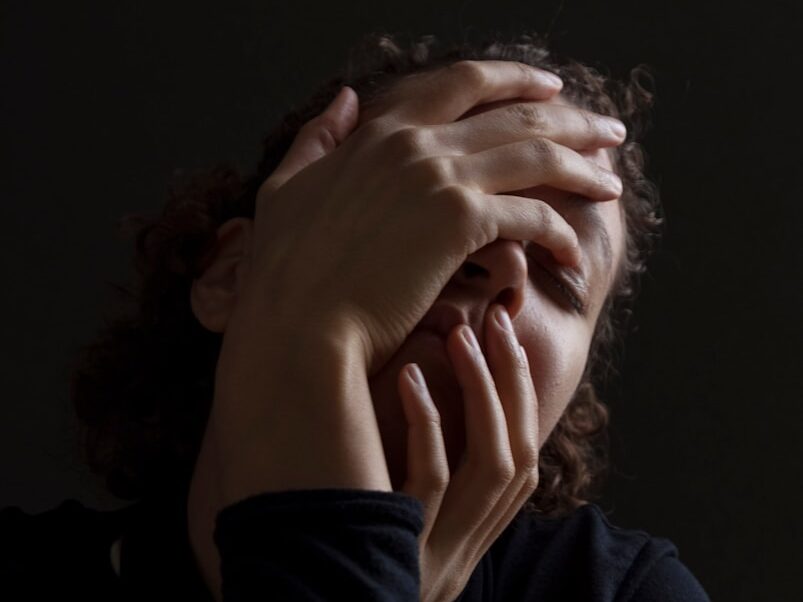 woman wearing blue long-sleeved shirt touching her face