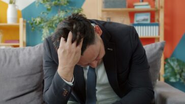 Man in suit sitting on couch with head in hands.