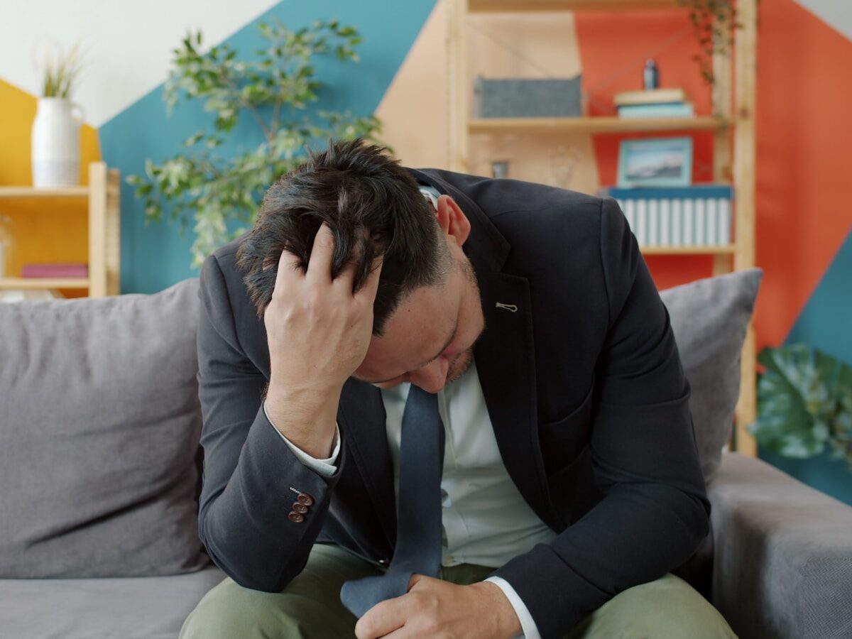 Man in suit sitting on couch with head in hands.