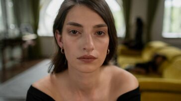 A close-up portrait of a woman with a calm expression, indoors, with thoughtful ambiance.