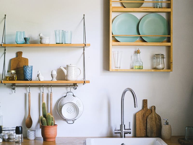 Cozy kitchen featuring rustic open shelving, green plants, and elegant dishware.