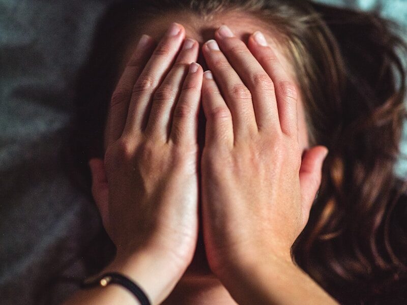 woman covering face lying on gray bed