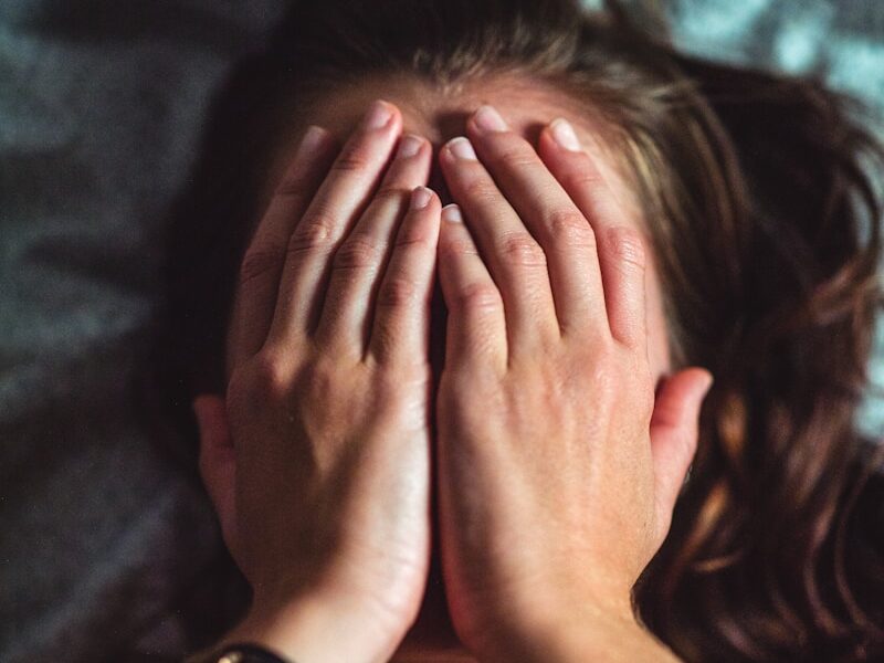 woman covering face lying on gray bed