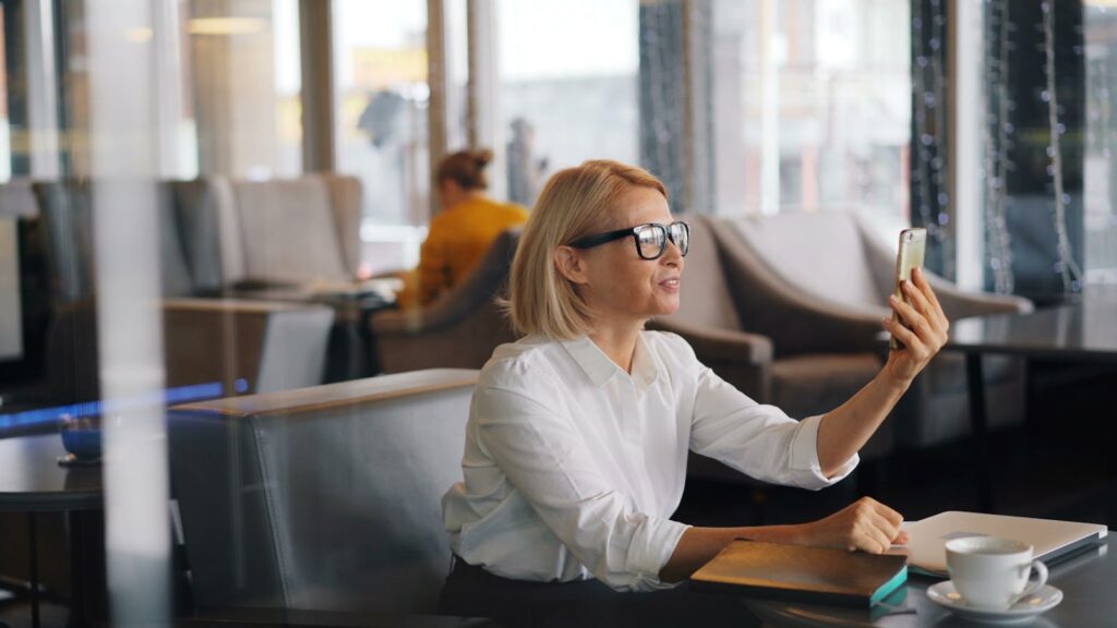 Smiling businesswoman having a video call in a modern café setting, enjoying a coffee break.