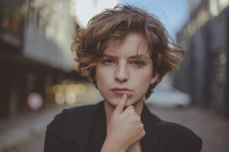 Close-up portrait of a woman with short hair, looking thoughtful in an urban setting.