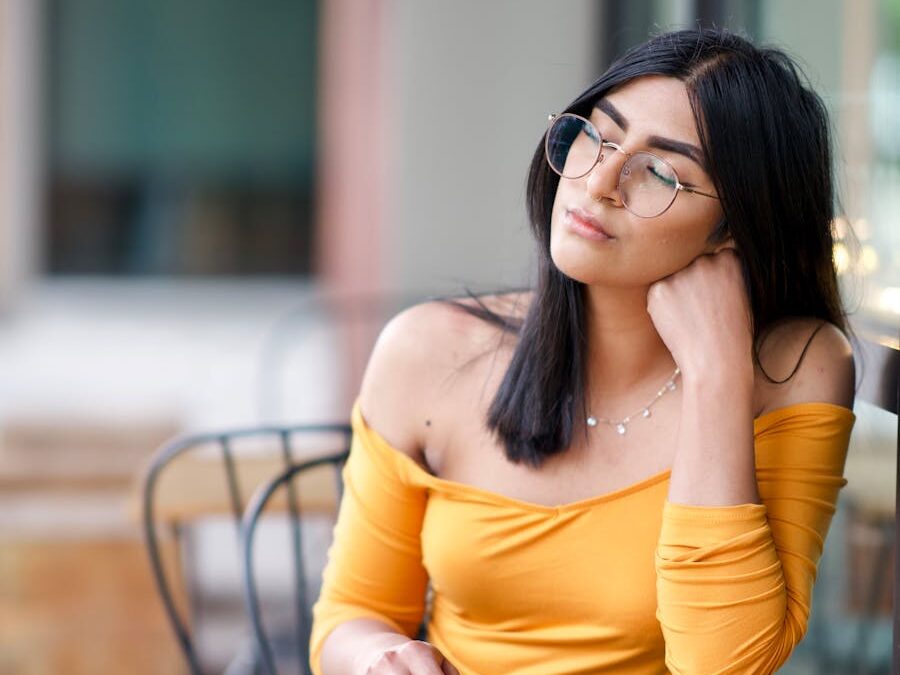 A thoughtful young woman in yellow, sitting at a table, lost in contemplation.