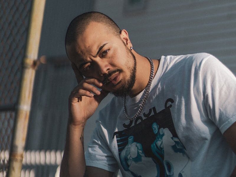 Portrait of a man outdoors in an urban setting, showcasing a pensive expression and fashion style.