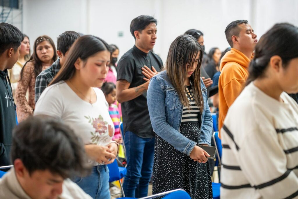 A diverse group of young adults engaged in a prayer gathering indoors in Ciudad de México.
