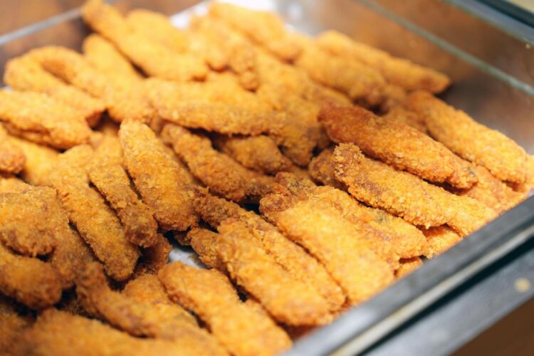 Golden brown breaded fish sticks neatly arranged in a metal tray, perfect for buffets or gatherings.