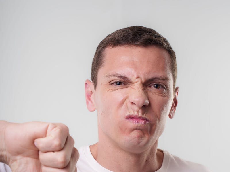 Adult male making a thumbs down gesture with a displeased expression indoors.