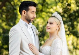 Beautiful outdoor wedding portrait featuring bride in lace gown and groom in suit.
