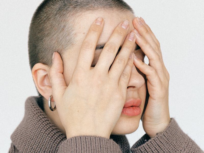 Close-up of a woman covering her face peacefully, wearing a knitted sweater.