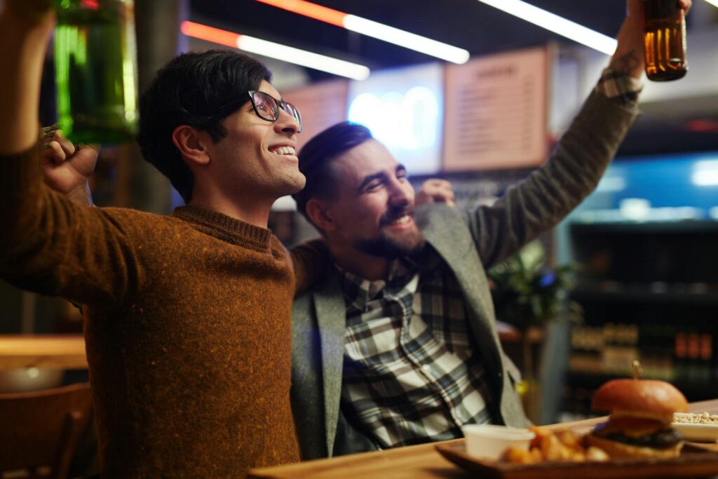 Two friends joyfully celebrating with beer in a lively bar setting.