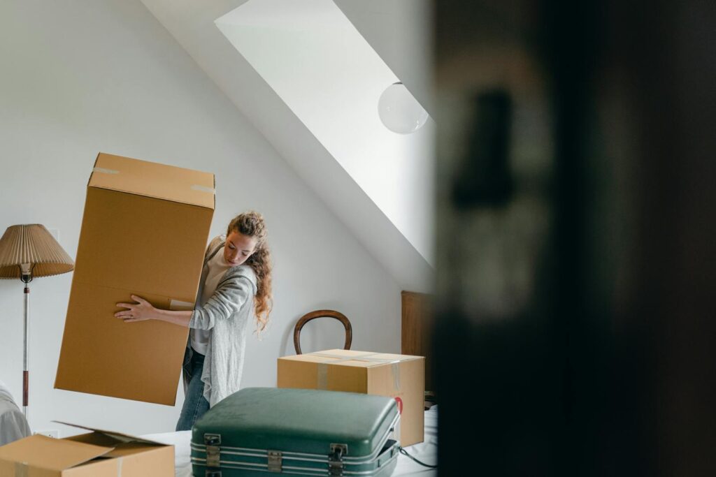 Woman preparing for relocation by packing boxes in a cozy, sunlit room with minimal furniture.