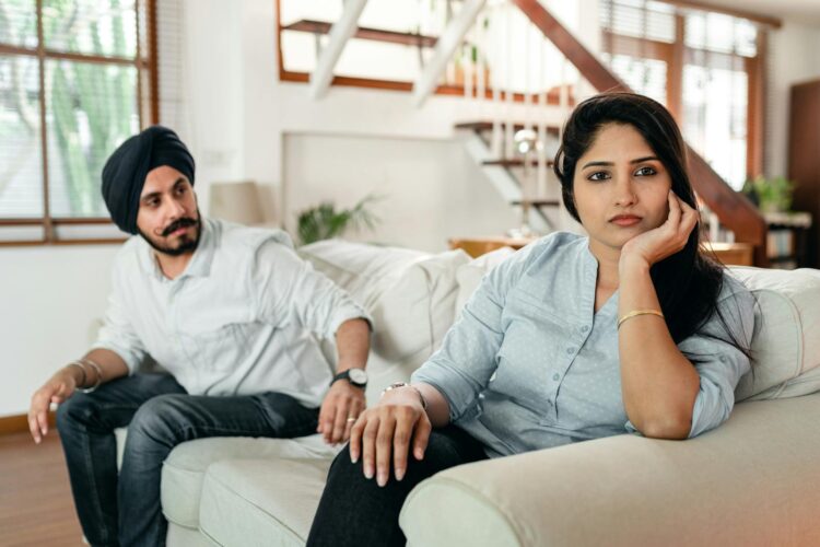 A thoughtful couple sits silently on a sofa, contemplating their relationship in a modern home.