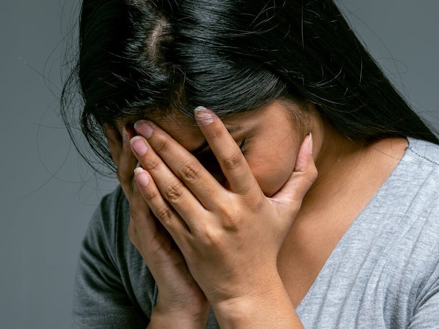 A woman hides her face in hands showing deep emotion and sadness in a studio setting.