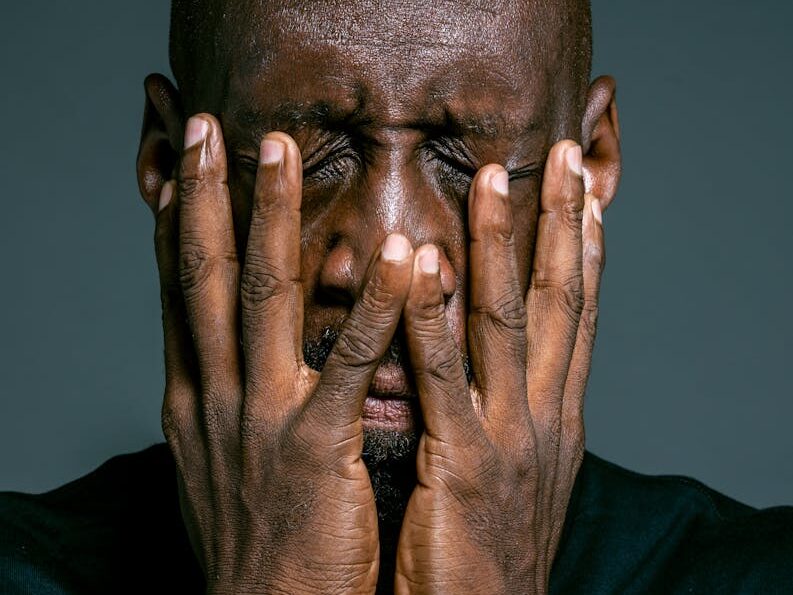 Portrait of a stressed African American man with hands on face expressing frustration.
