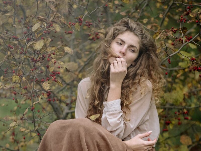 Thoughtful woman sitting on a tree stump in an autumnal forest, lost in deep reflection.