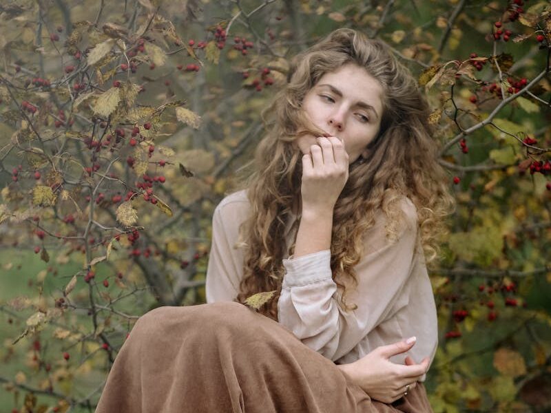 Thoughtful woman sitting on a tree stump in an autumnal forest, lost in deep reflection.