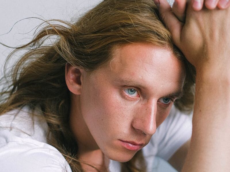 A young man with long hair sits pensively, showcasing a serene and thoughtful expression in a studio setting.