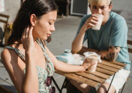 Young tender dreamy girlfriend and Asian pensive boyfriend with cup of hot coffee on sunny street
