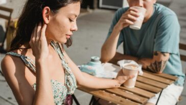 Young tender dreamy girlfriend and Asian pensive boyfriend with cup of hot coffee on sunny street