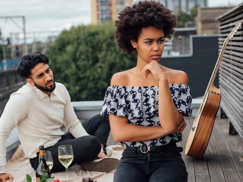 Couple having a romantic picnic on a rooftop, featuring wine, red roses, and an acoustic guitar.