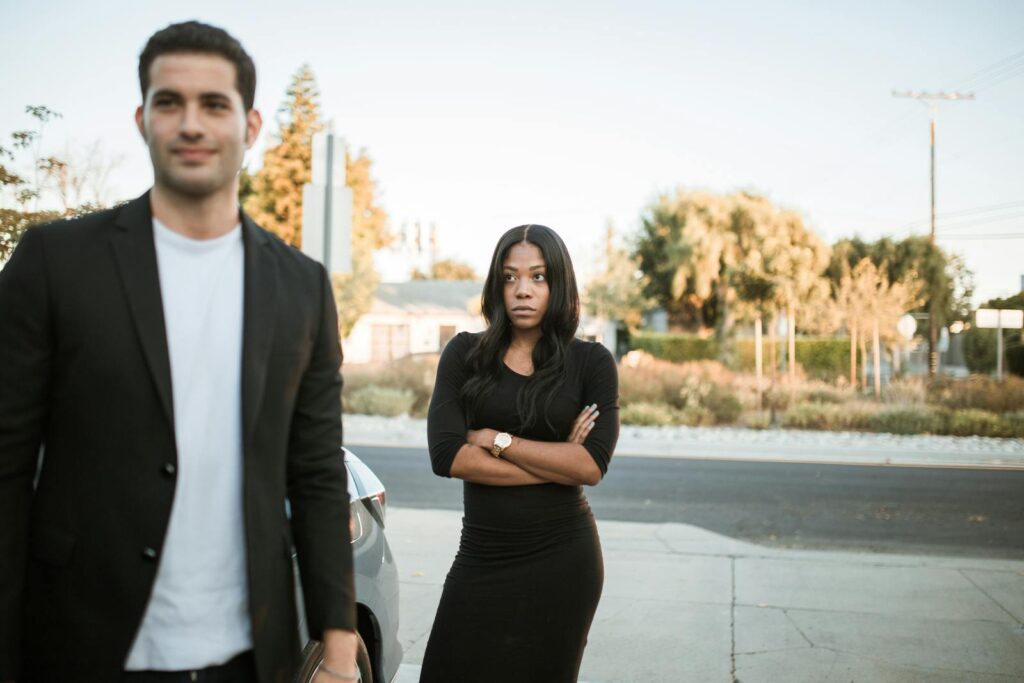 A couple facing relationship tension outdoors with arms folded, expressing emotions.