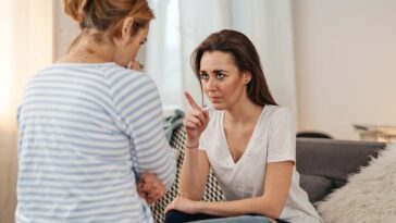 Two women having a serious conversation in a cozy living room setting.