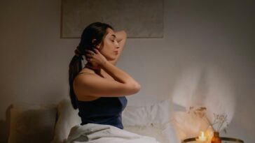 A calm woman sits on a bed in a cozy bedroom, enjoying a peaceful moment.