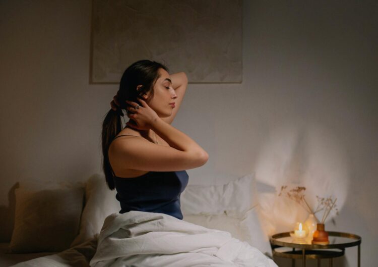 A calm woman sits on a bed in a cozy bedroom, enjoying a peaceful moment.