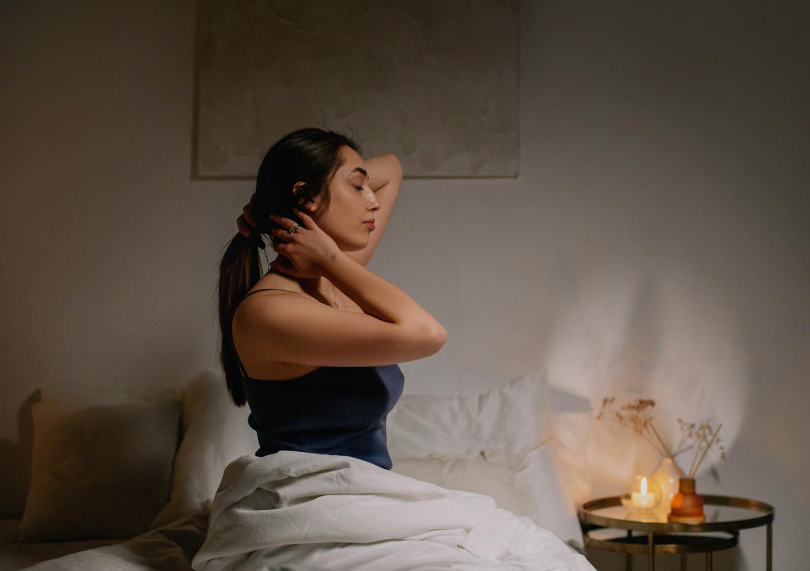 A calm woman sits on a bed in a cozy bedroom, enjoying a peaceful moment.