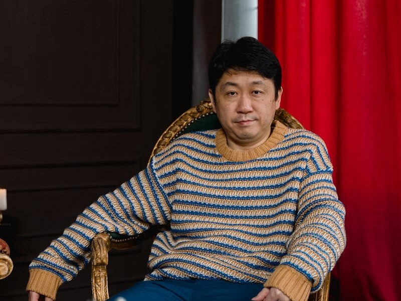 Man in a striped sweater sitting near a chessboard, pondering a move.