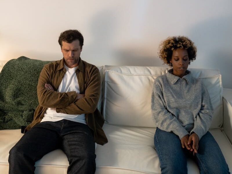 A couple experiencing tension, sitting apart on a sofa indoors.