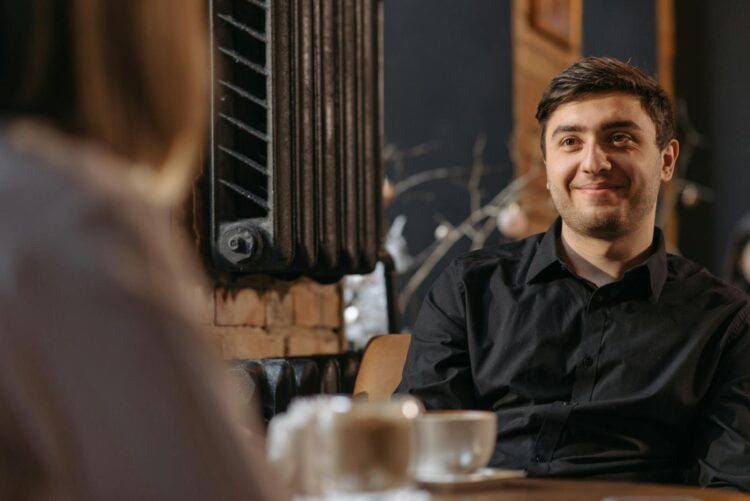 Young man in a black shirt enjoying a conversation in a cozy cafe.