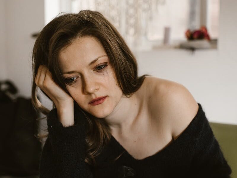A thoughtful woman sits indoors, holding a cup of coffee, reflecting.