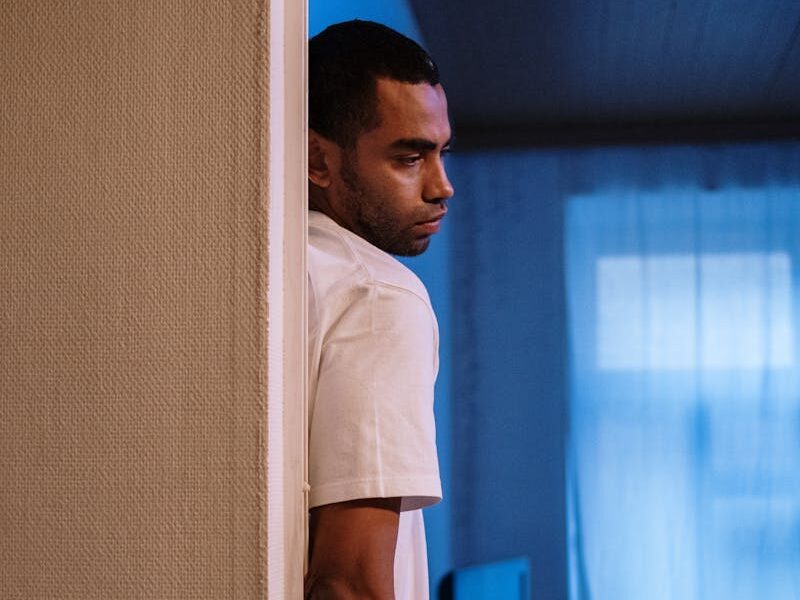 A man stands pensively in a dimly lit room, capturing a moment of deep thought.