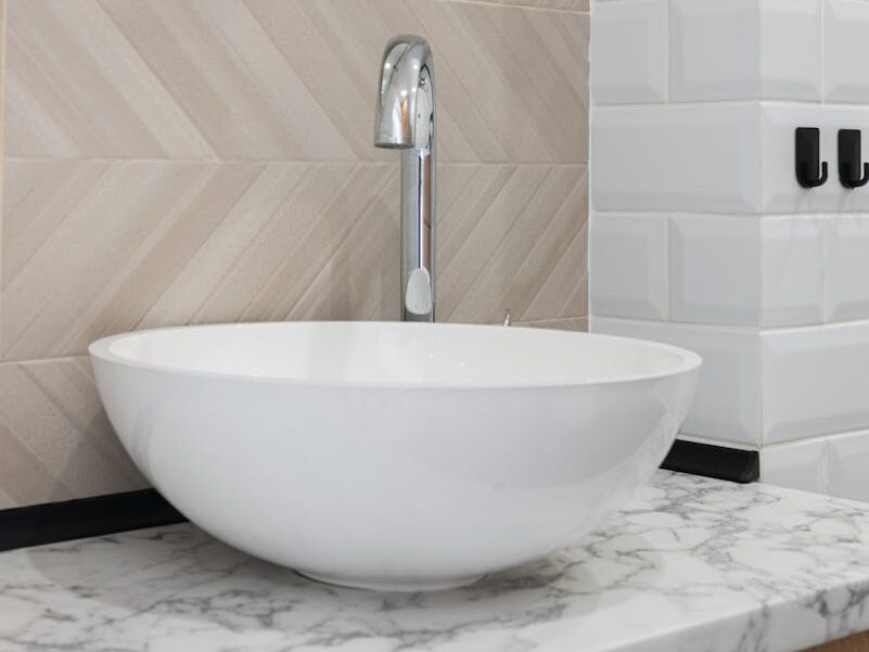Interior of light modern restroom with sink and faucet on cabinet under mirror on tile wall