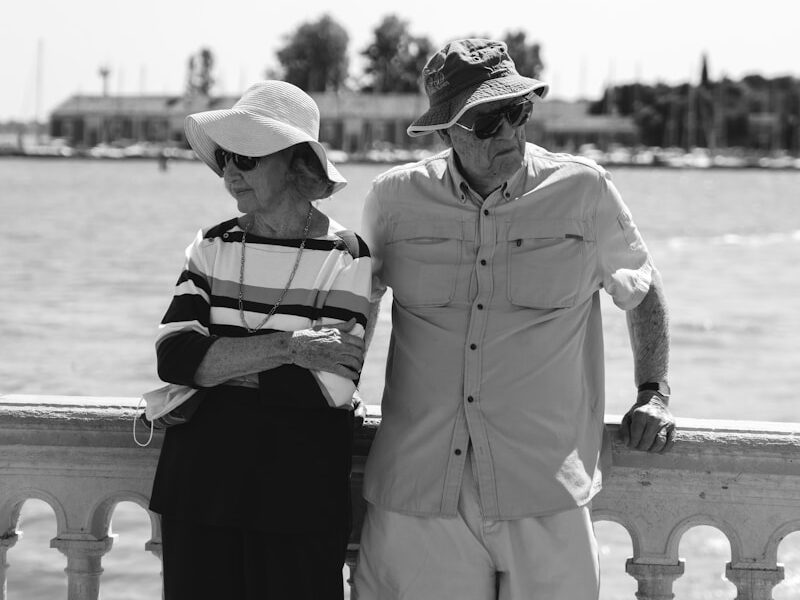 grayscale photo of man in button up shirt and black pants sitting on concrete bench