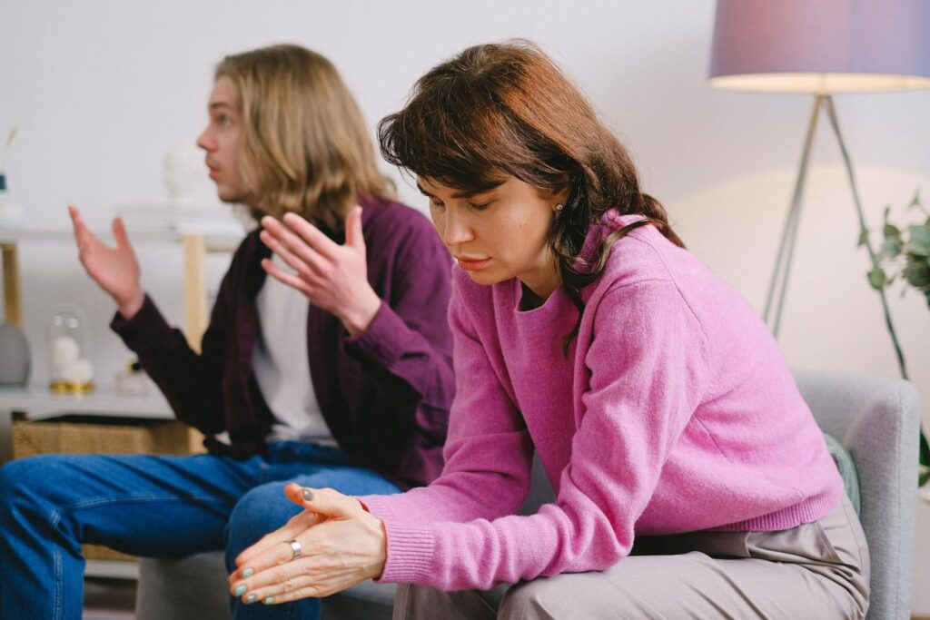 A couple having a serious discussion indoors; one looks upset while the other gestures expressively.
