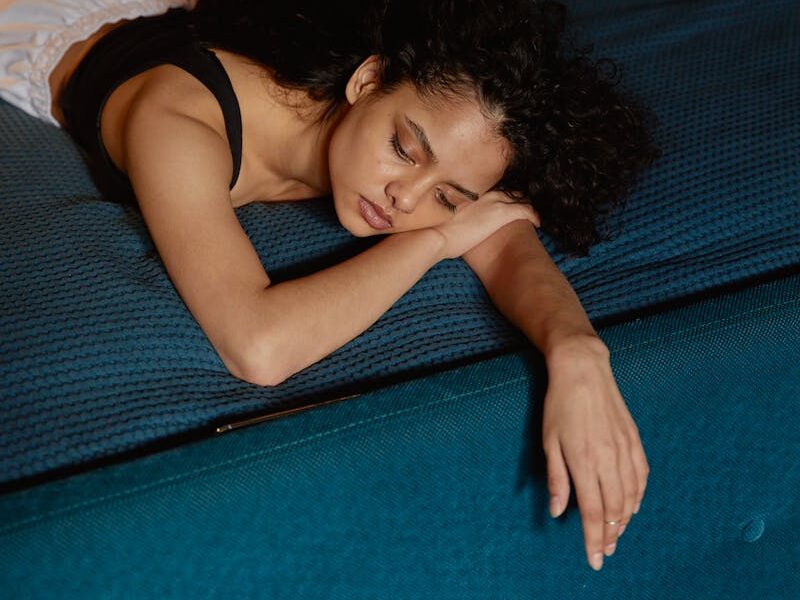 Thoughtful woman with curly hair lying on bed, expressing contemplation and calmness.