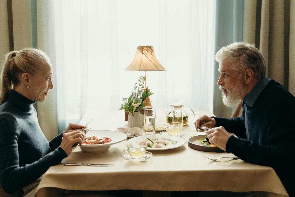 Elderly couple enjoying a meal together in a cozy, warmly lit indoor setting.