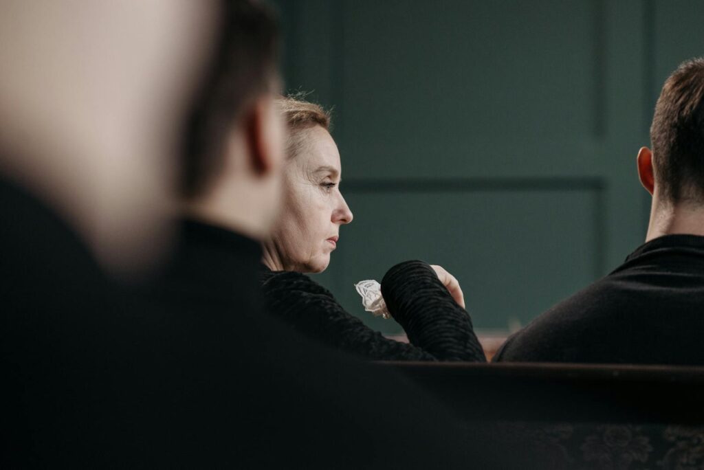A solemn moment as a woman reflects during an indoor gathering, evoking themes of loss and sorrow.