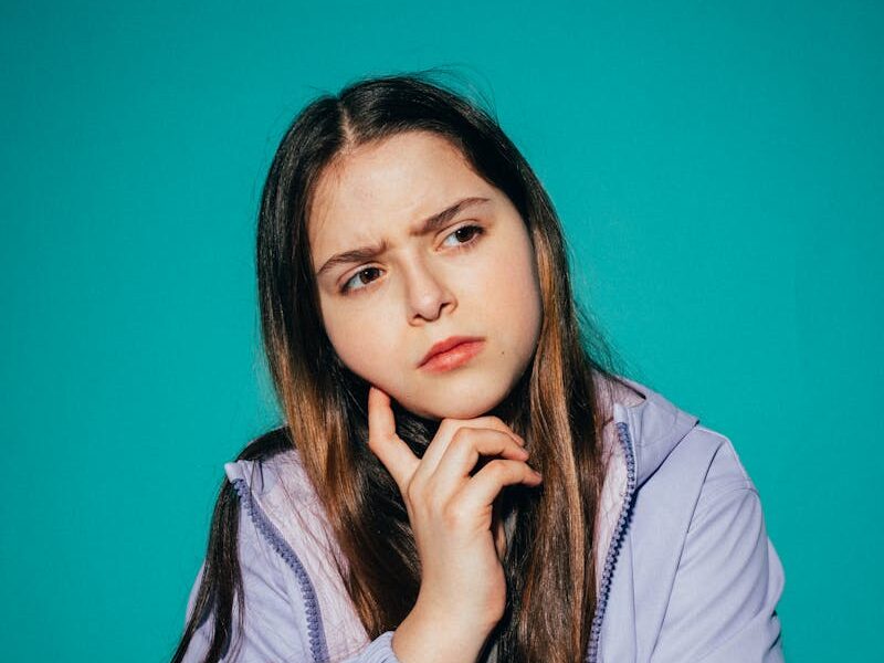 A young girl pondering deeply against a vibrant teal background.