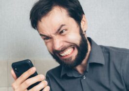 Adult male in frustration holding a smartphone inside an office setting.