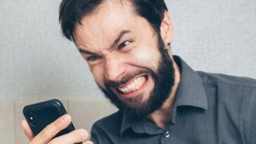 Adult male in frustration holding a smartphone inside an office setting.
