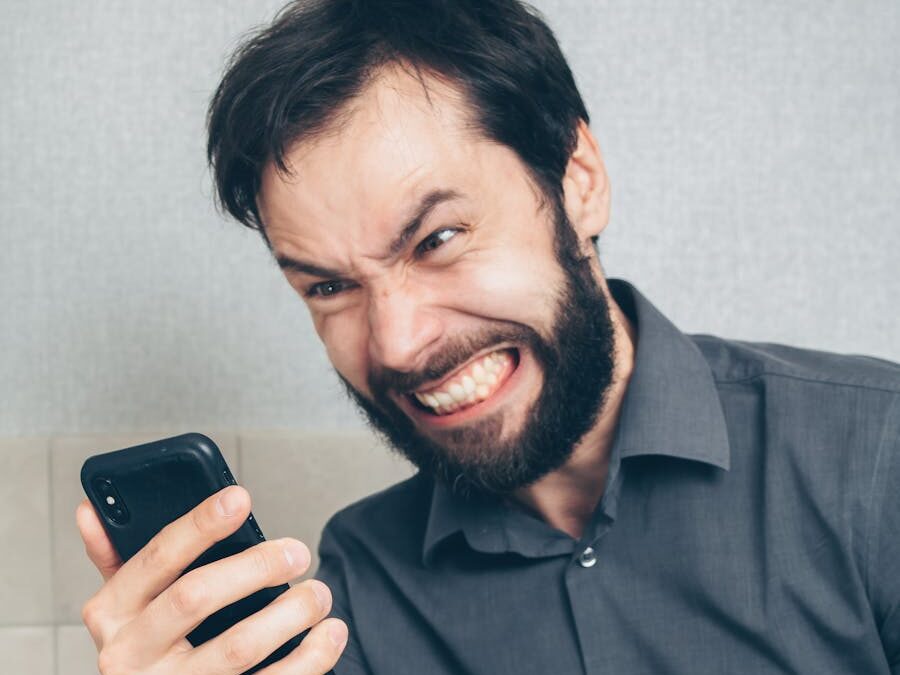 Adult male in frustration holding a smartphone inside an office setting.